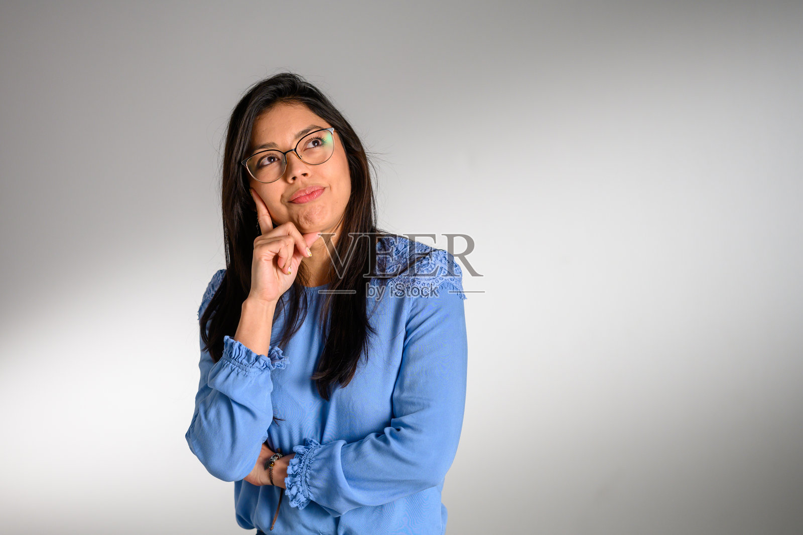 戴眼镜的深思熟虑的西班牙裔女性穿着蓝色上衣照片摄影图片