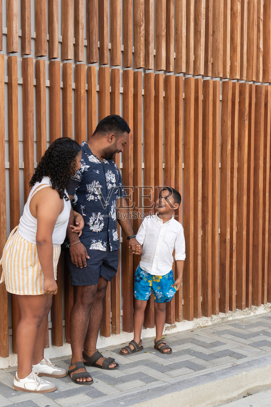 快乐的家庭在木墙前手牵手，互相微笑。照片摄影图片