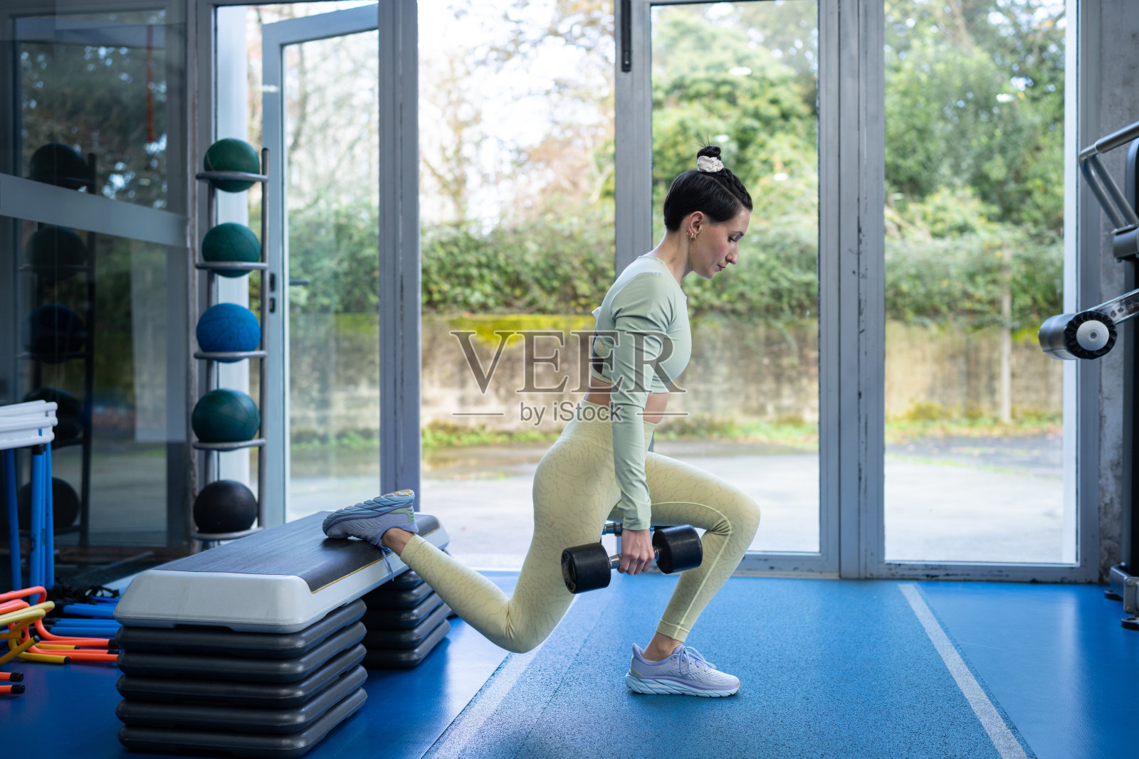 决心坚定的年轻女性在健身房举重并进行保加利亚分腿深蹲，致力于增强力量和提升整体健康，同时专注于自己的目标。照片摄影图片