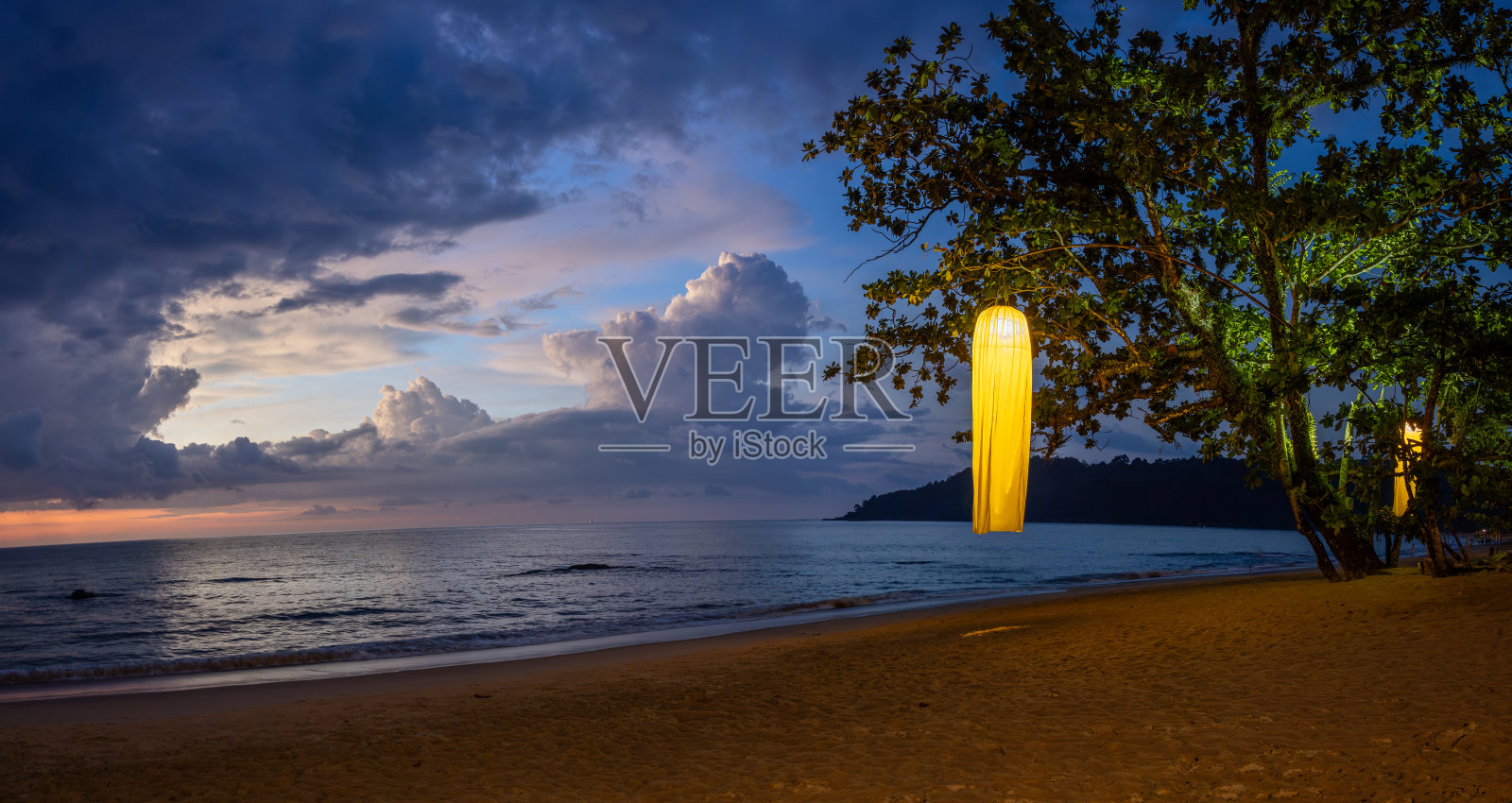 泰国考拉克海岸的日落。海滩上树上挂着的灯。照片摄影图片