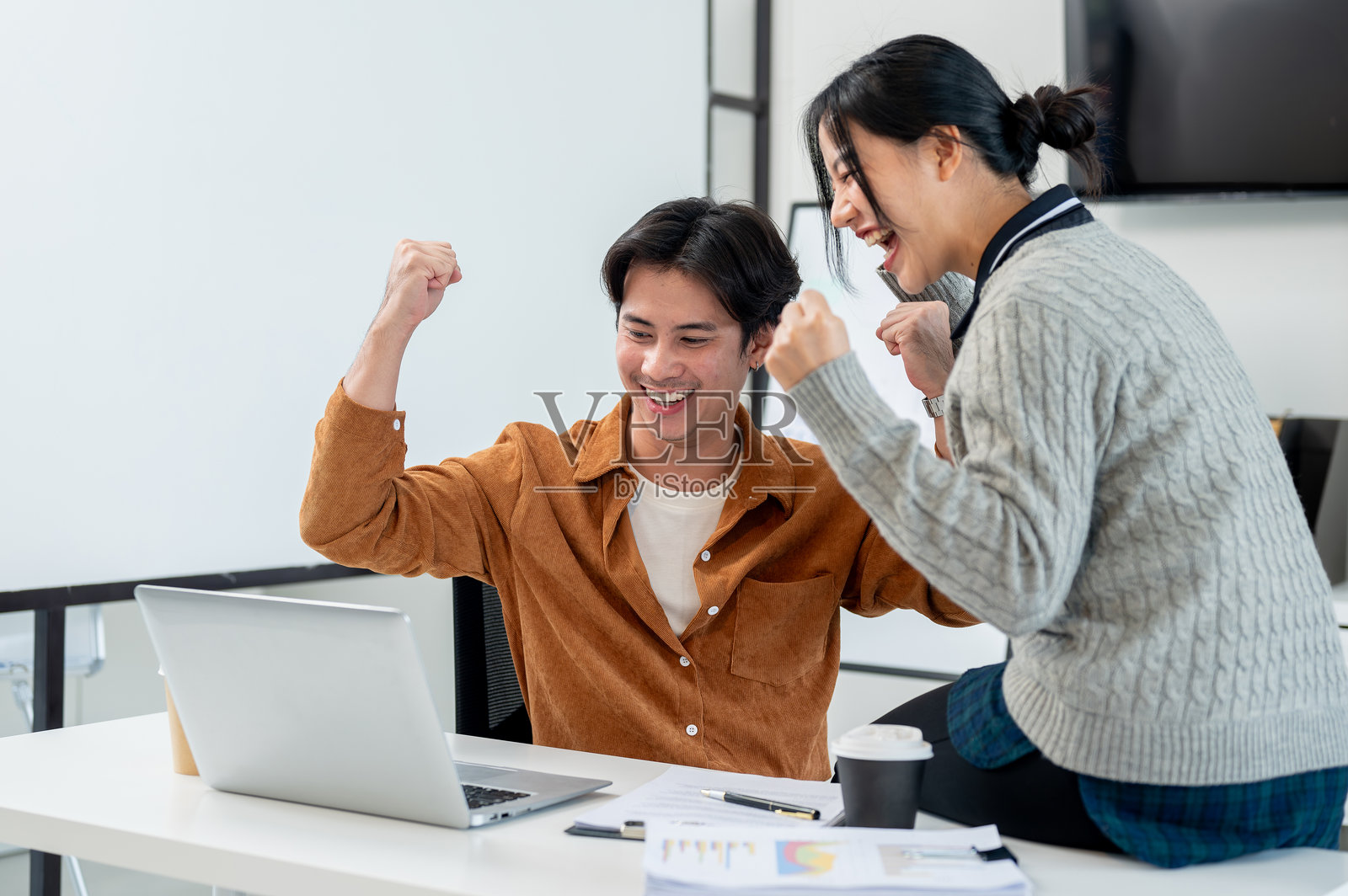 两位快乐的亚洲商务人士举起胜利的拳头，注视着笔记本电脑屏幕。照片摄影图片