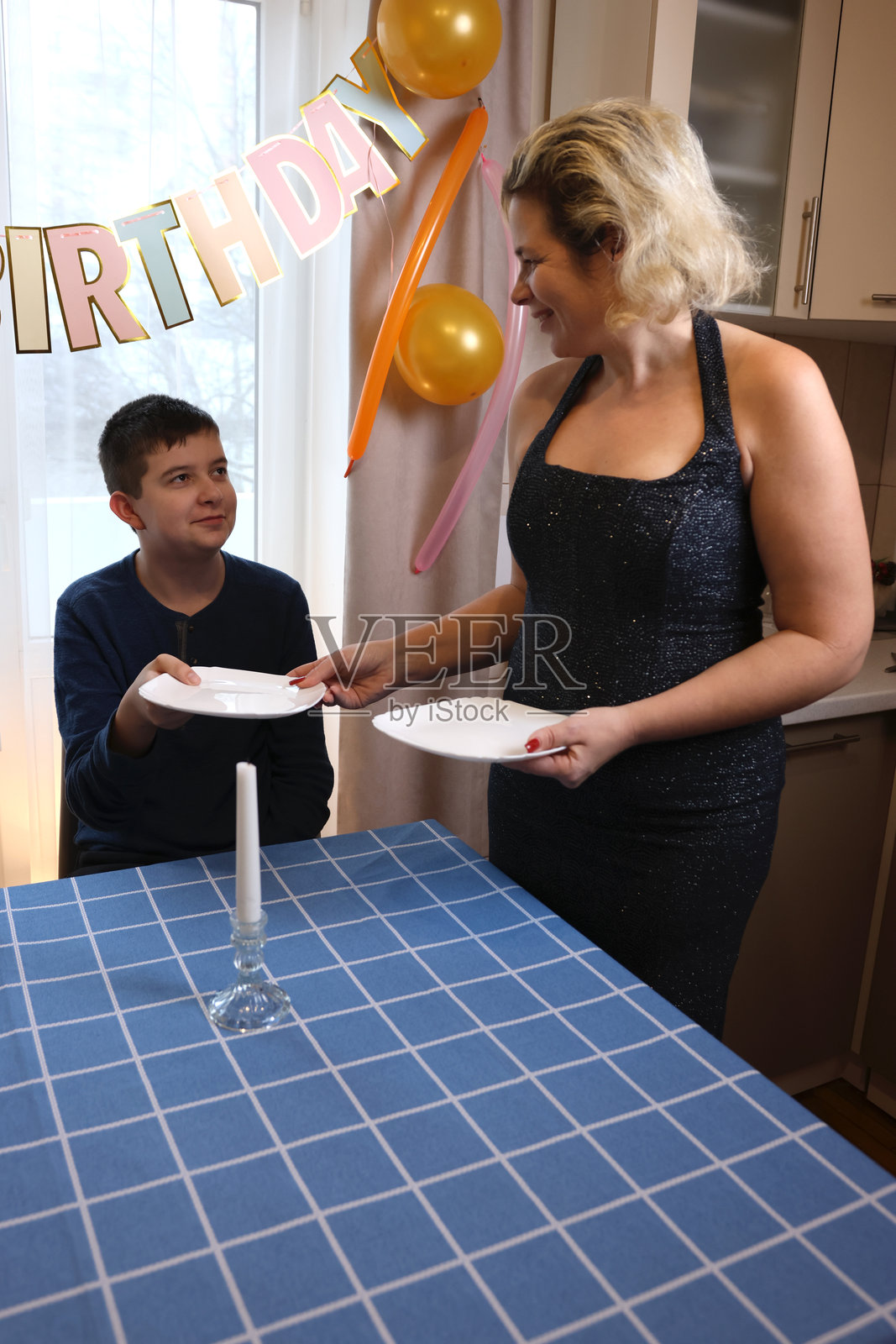一位母亲与她的儿子和侄子一起为生日庆祝活动装饰房间和节日餐桌。柔和的灯光。照片摄影图片