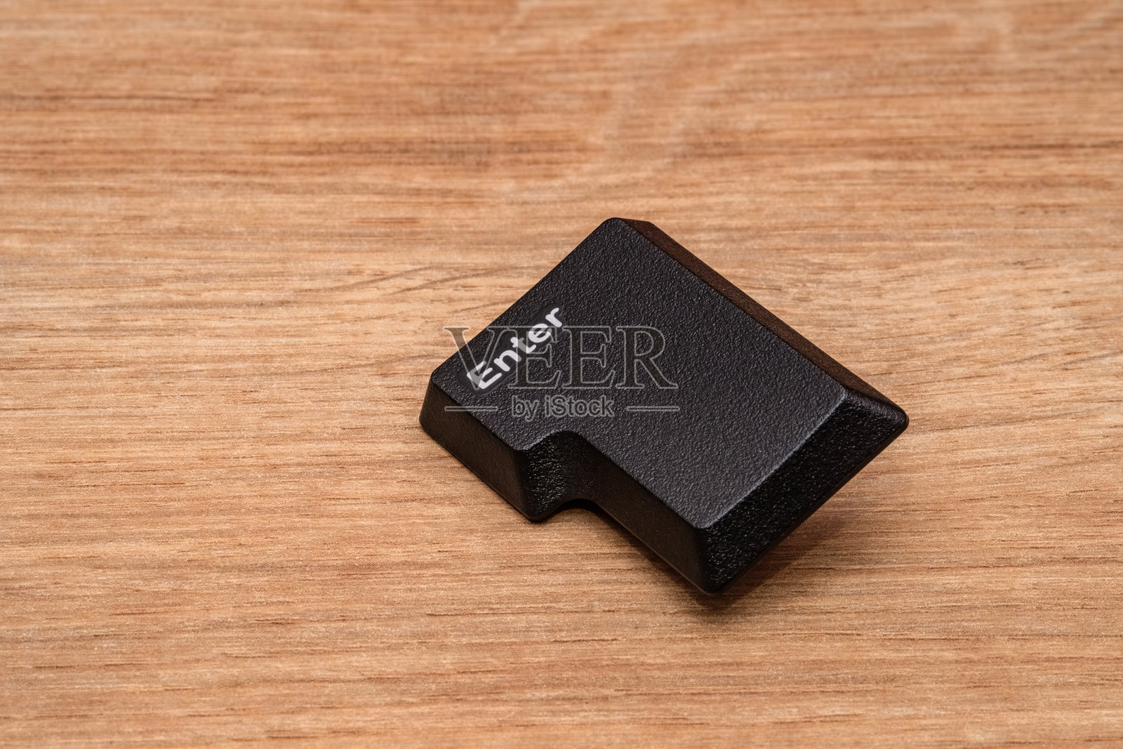 从键盘上拆下的回车键，放置在木质表面上。照片摄影图片