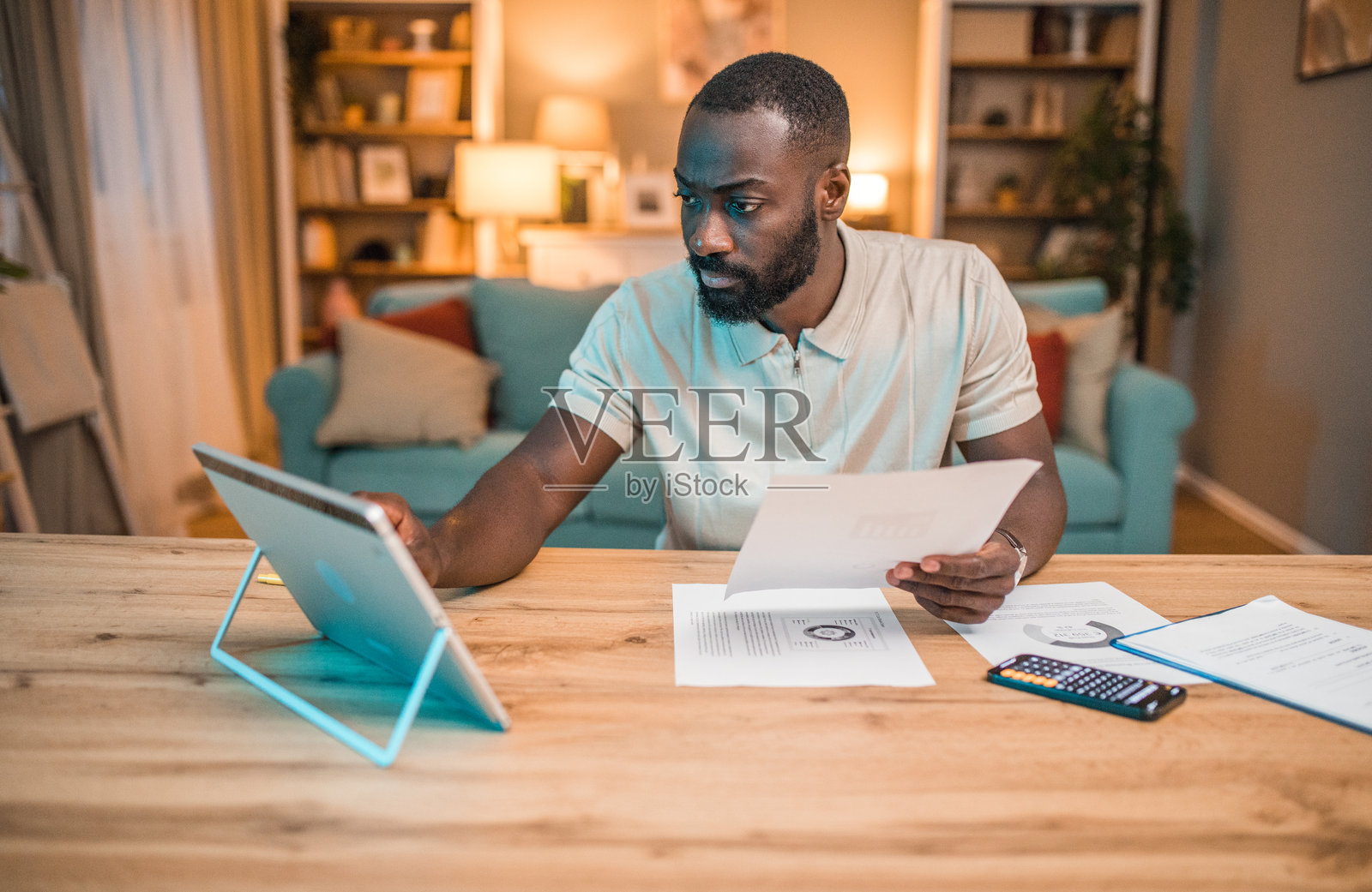 一位黑人男性坐在餐桌旁使用数字平板进行电子银行和支付账单。照片摄影图片