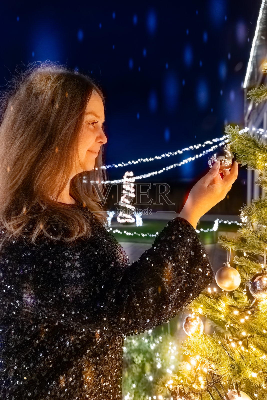 女人在节日的户外环境中，夜晚为圣诞树装饰饰品照片摄影图片