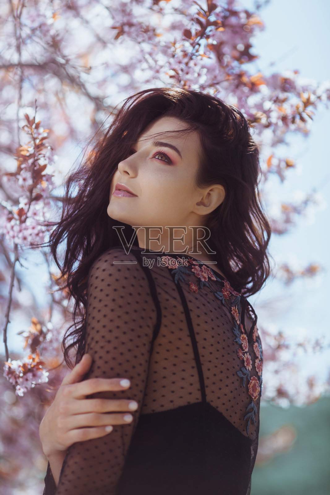 穿着花卉黑色连衣裙的浪漫女性在樱花树下照片摄影图片