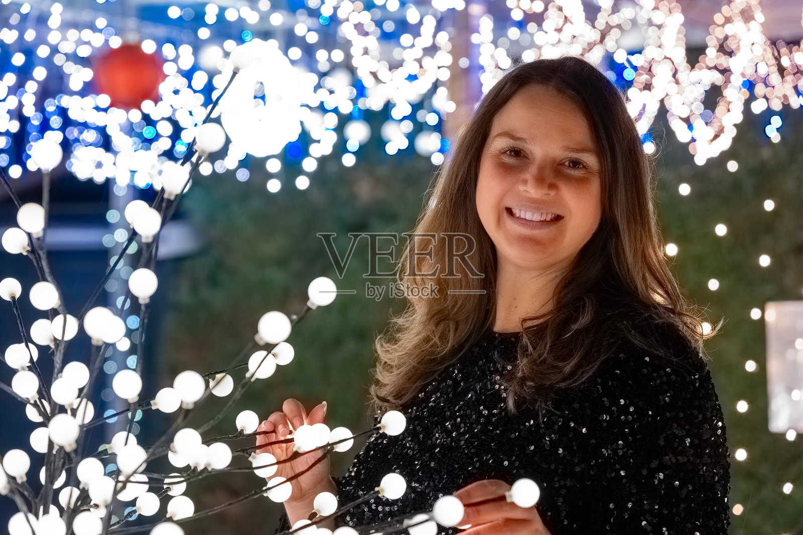 女人在节日装饰的环境中，微笑着被闪烁的节日灯光包围，夜晚时分。照片摄影图片