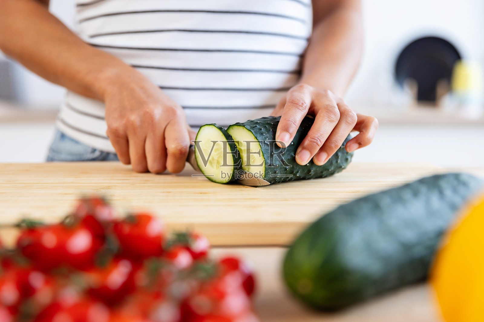 特写女性手在厨房的木砧板上切新鲜黄瓜照片摄影图片