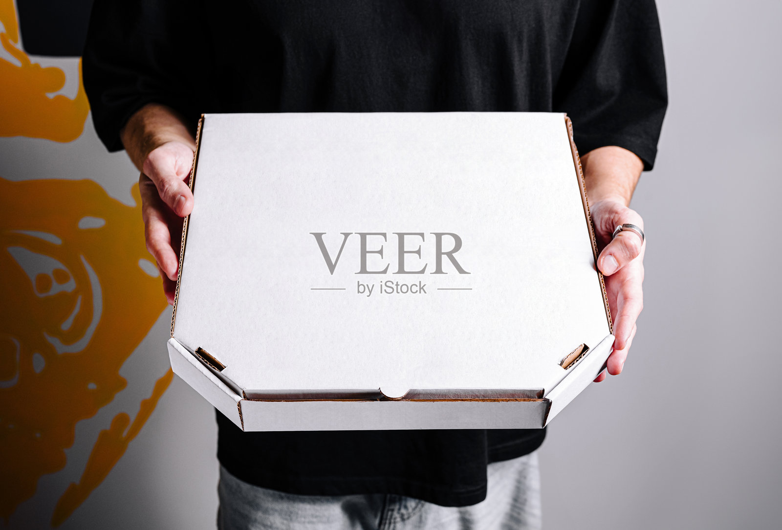 在休闲环境中，个人手持一个空白的白色披萨盒，背景是五彩斑斓的墙壁。照片摄影图片