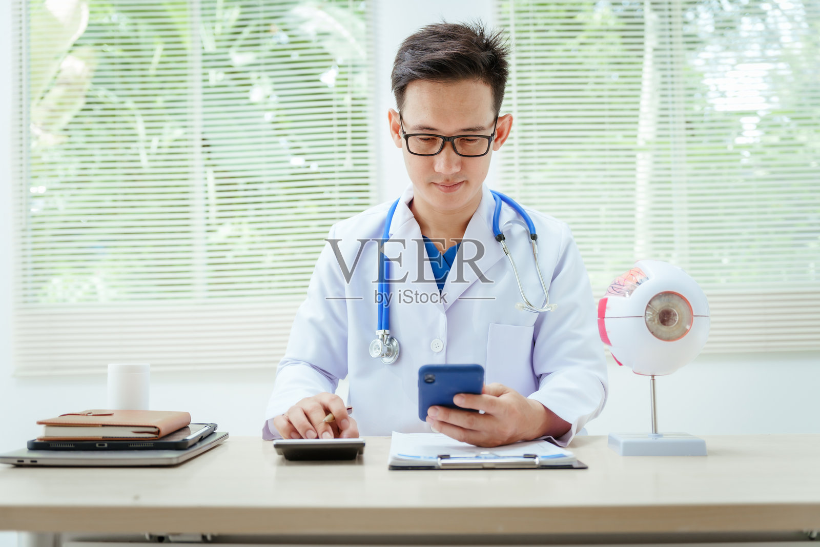 一位戴眼镜的男性医生坐在医院的桌子前，讲解青光眼、白内障、翼状胬肉和糖尿病视网膜病变等眼病。早期发现有助于防止视力丧失。照片摄影图片