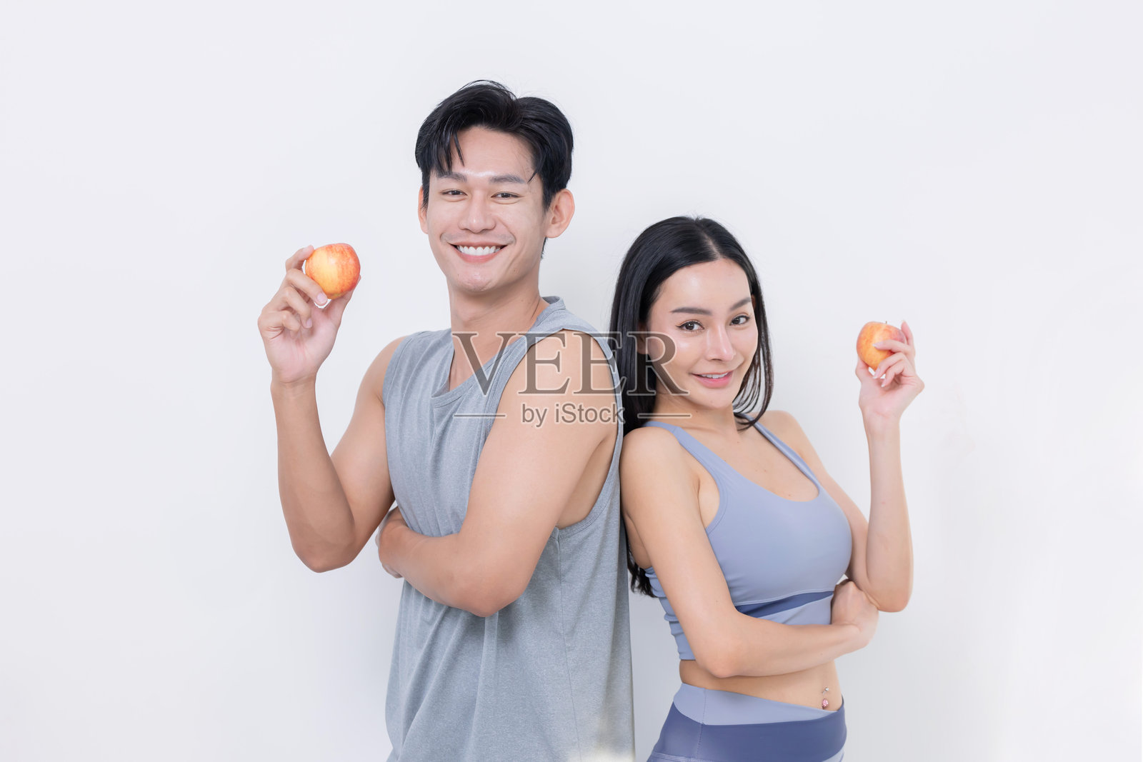 亚洲年轻情侣背对背微笑，手持苹果，传达健康生活方式的理念照片摄影图片