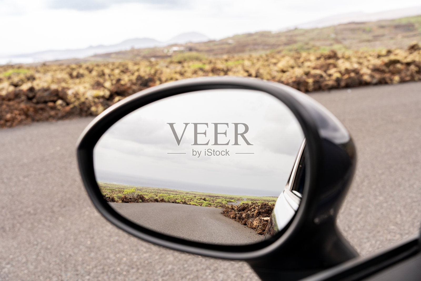 火山景观在汽车侧后视镜中倒影，捕捉到兰萨罗特崎岖的地形，展现了风景如画的岛屿公路之旅。照片摄影图片