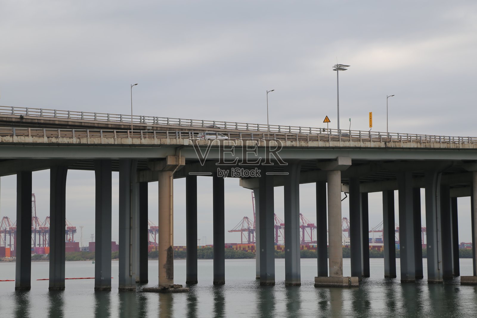 一座宽阔的桥梁，混凝土柱子延伸入海，通向一个工业港口照片摄影图片