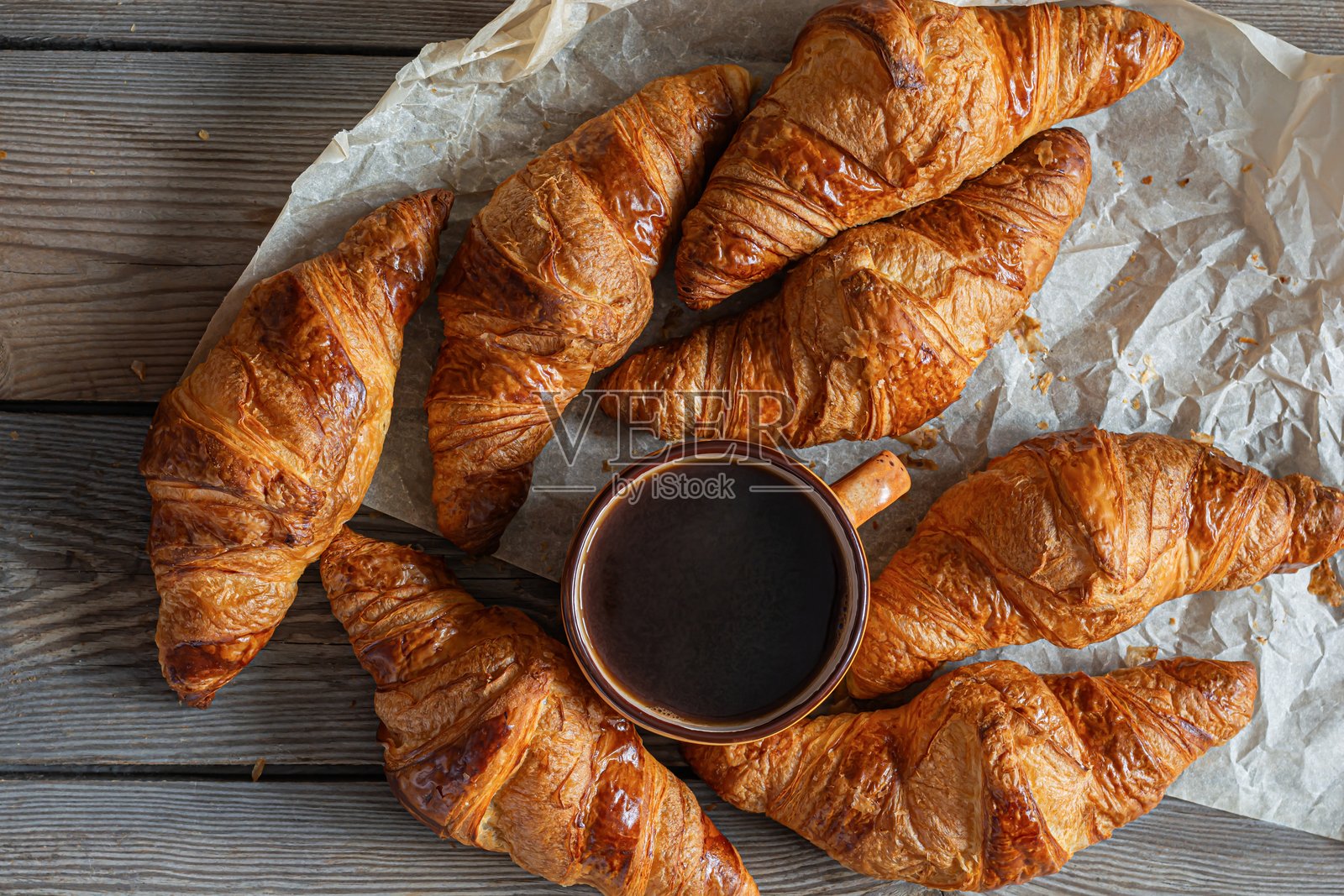 新鲜的可颂面包配一杯卡布奇诺（咖啡），背景为木质桌面。受欢迎的美味早餐。照片摄影图片