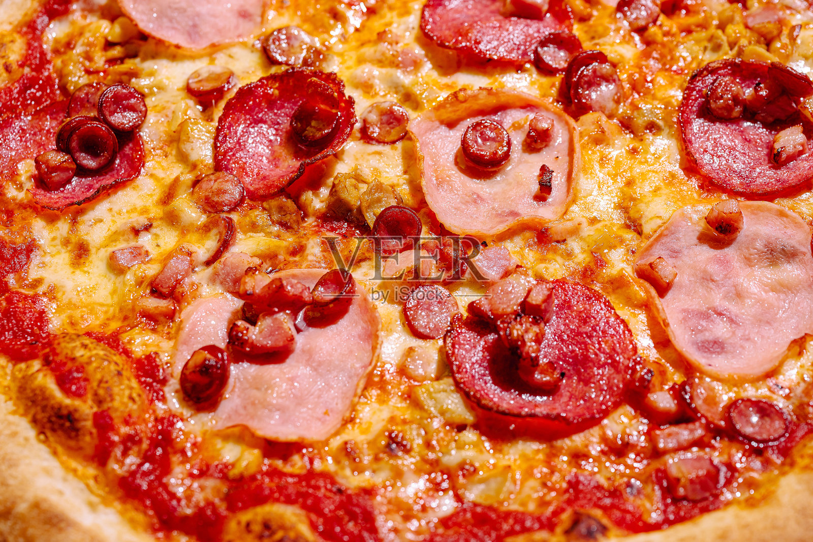 美味的刚出炉的比萨，上面铺满了意大利香肠、火腿和香肠，晚上在比萨店供应。照片摄影图片