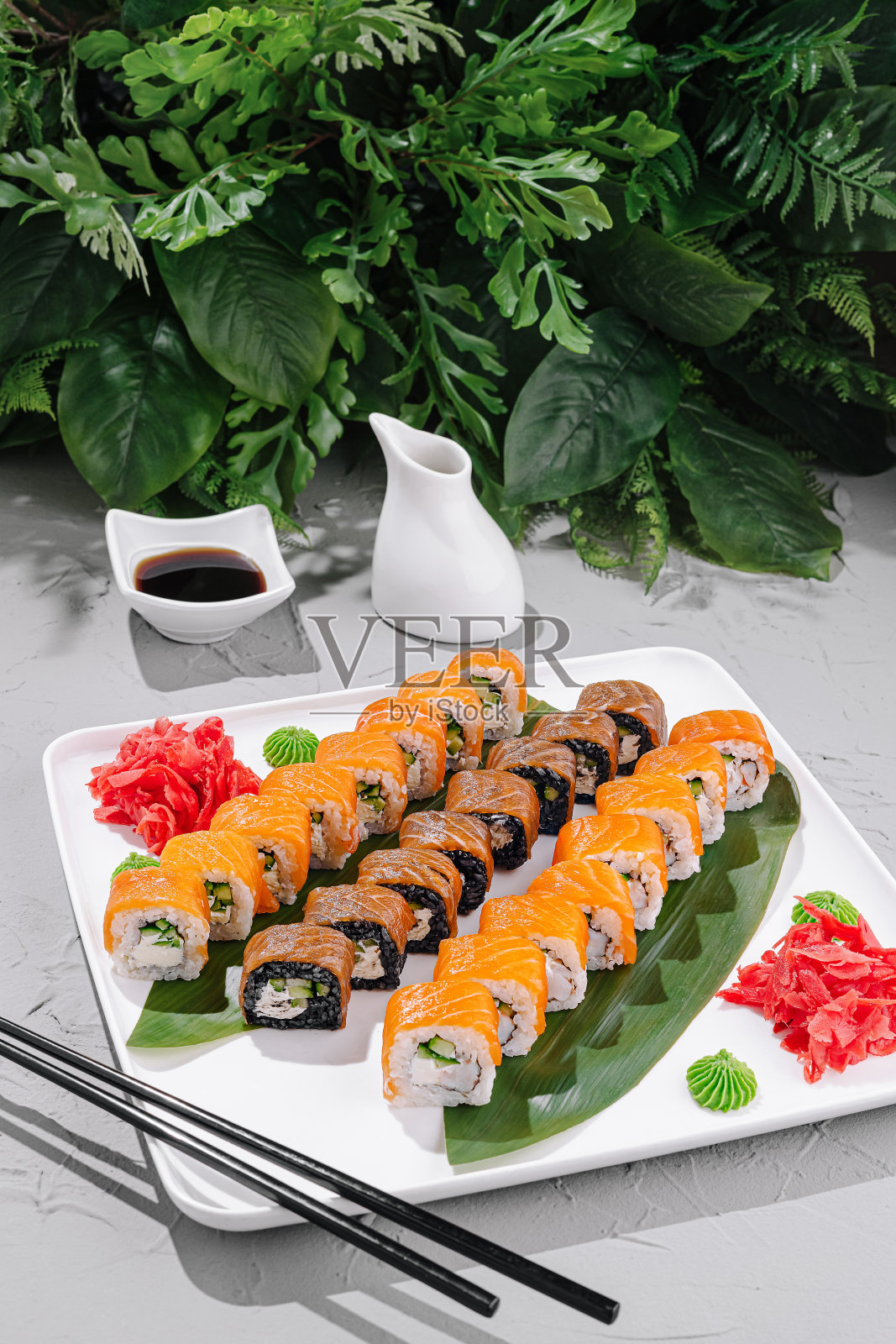 新鲜寿司拼盘摆放在白色盘子上，配有装饰和酱汁，背景是灰色台面。照片摄影图片