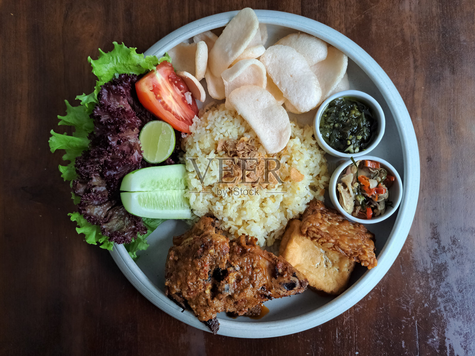 美味的塔利旺烤鸡或龙目岛蒜蓉黄油饭，炸脆的天贝和豆腐，虾片，新鲜蔬菜，青辣椒酱，马塔酱。印尼美食菜单。照片摄影图片