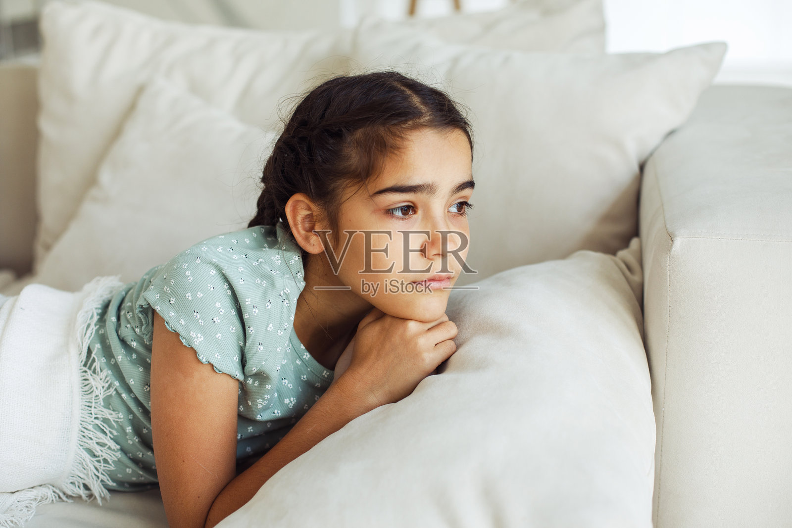 一个十岁的小女孩扎着辫子，正躺在沙发上。照片摄影图片