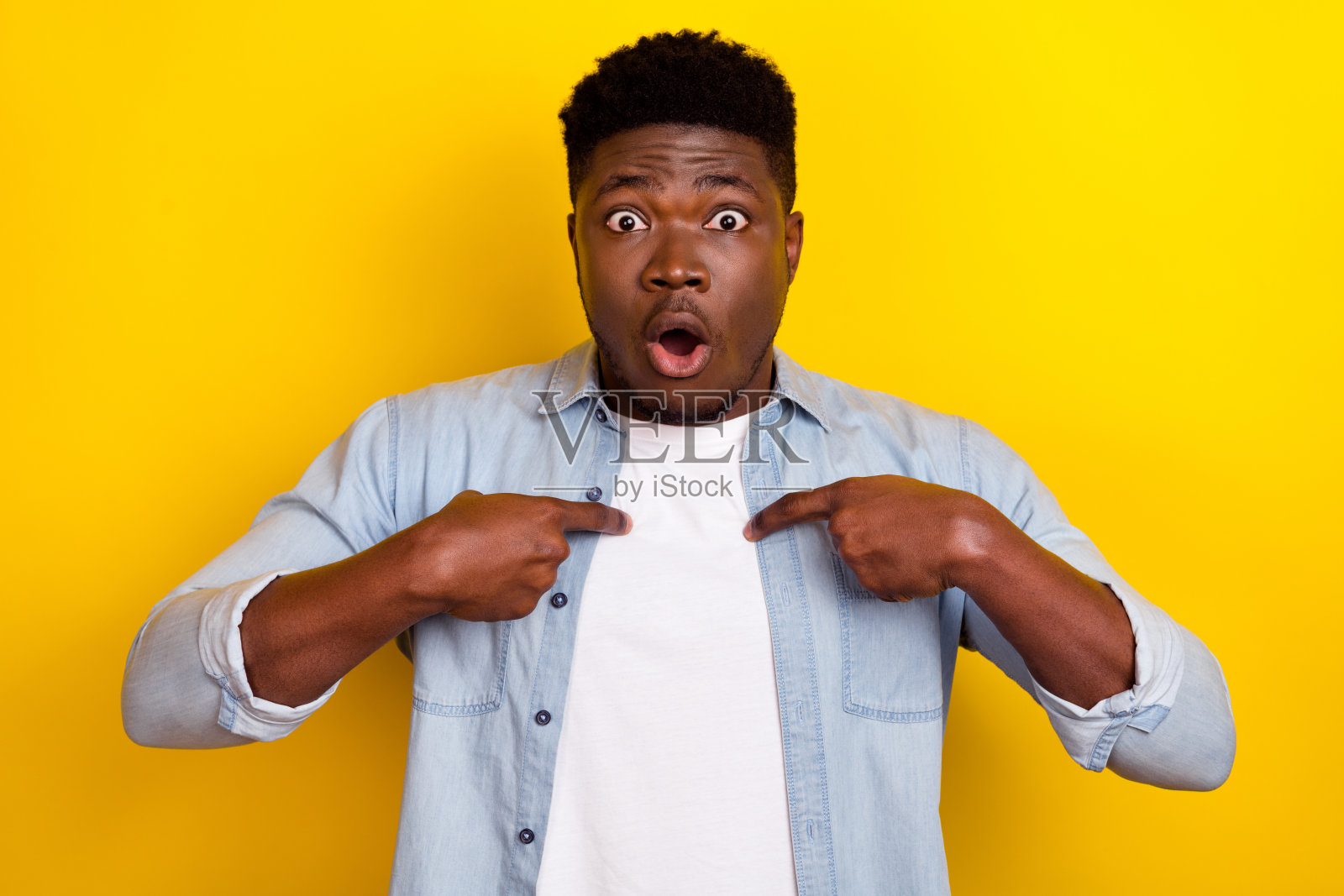 一位年轻的棕发男士在黄色背景下穿着牛仔裤和衬衫，显得很紧张。照片摄影图片