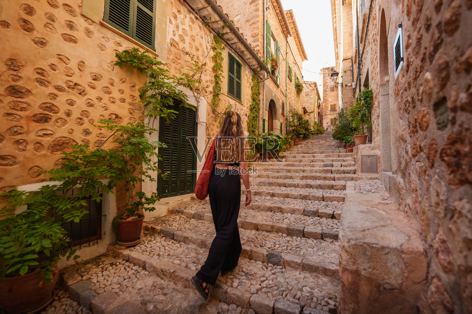 一位旅行者攀登着马洛卡福尔纳卢奇的风景如画的石阶，周围是乡村风格的地中海建筑、郁郁葱葱的绿意和温暖的阳光。照片摄影图片