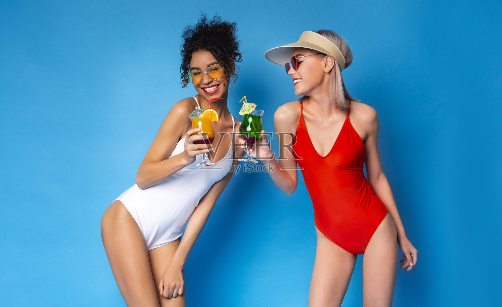 朋友们穿着泳衣在蓝色背景下享受五彩缤纷的鸡尾酒照片摄影图片