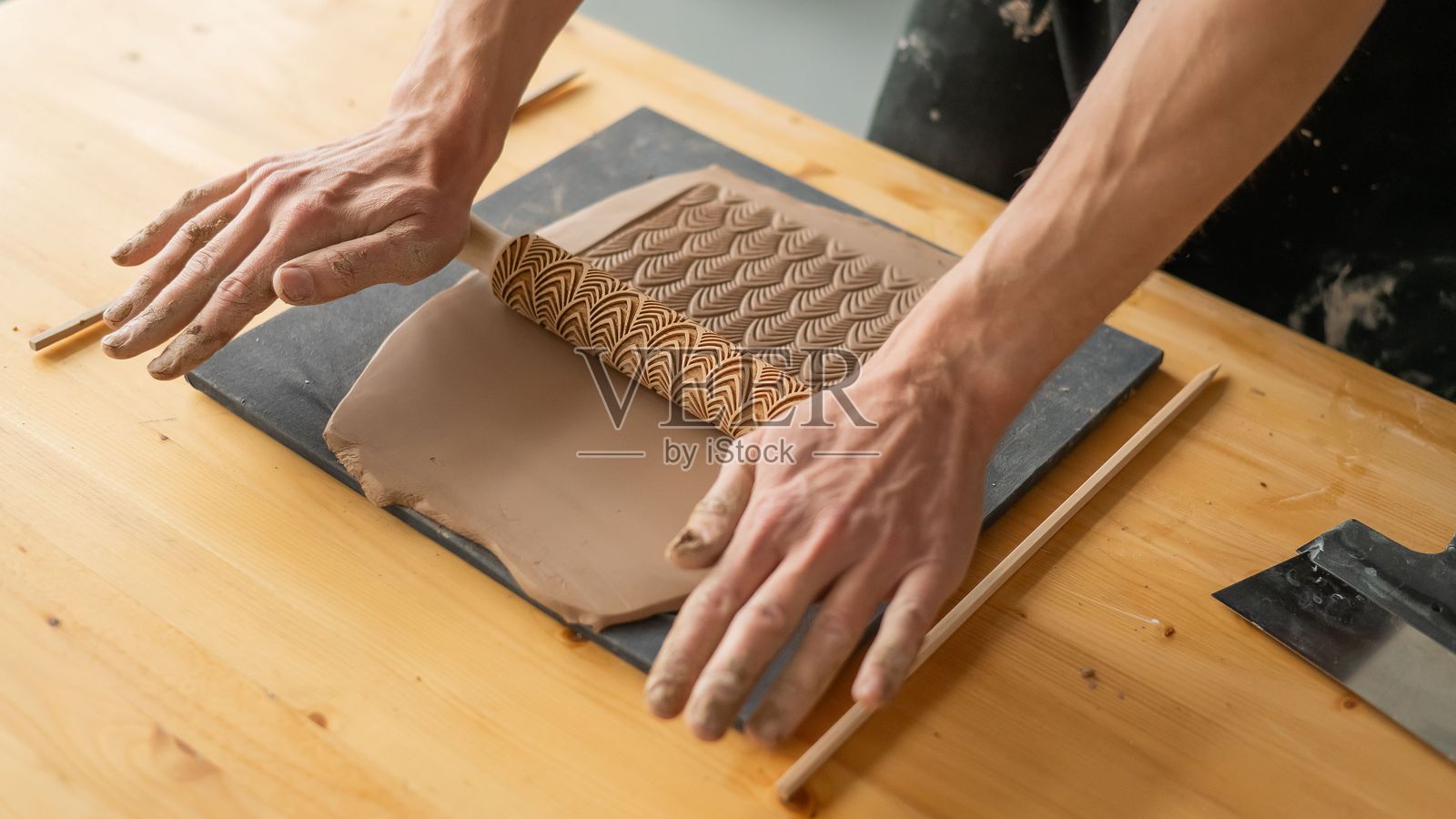 陶艺师的手在使用带有图案的擀面杖擀制粘土的特写镜头。照片摄影图片