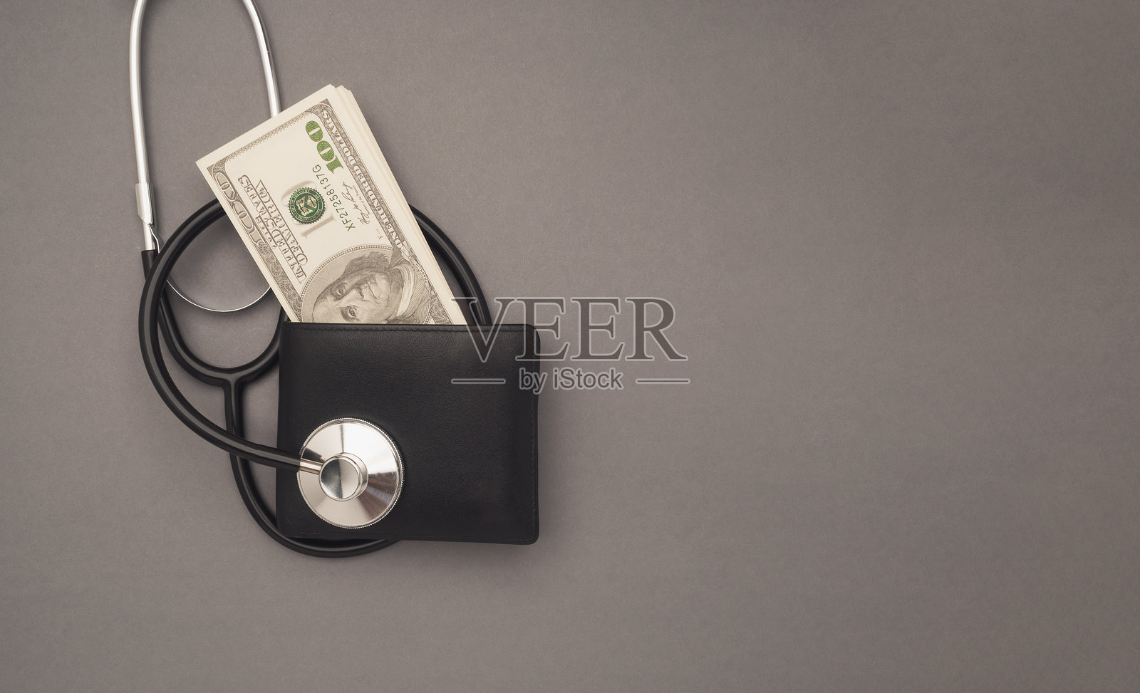 灰色背景上用听诊器检查钱包。医疗费用和健康投资。照片摄影图片