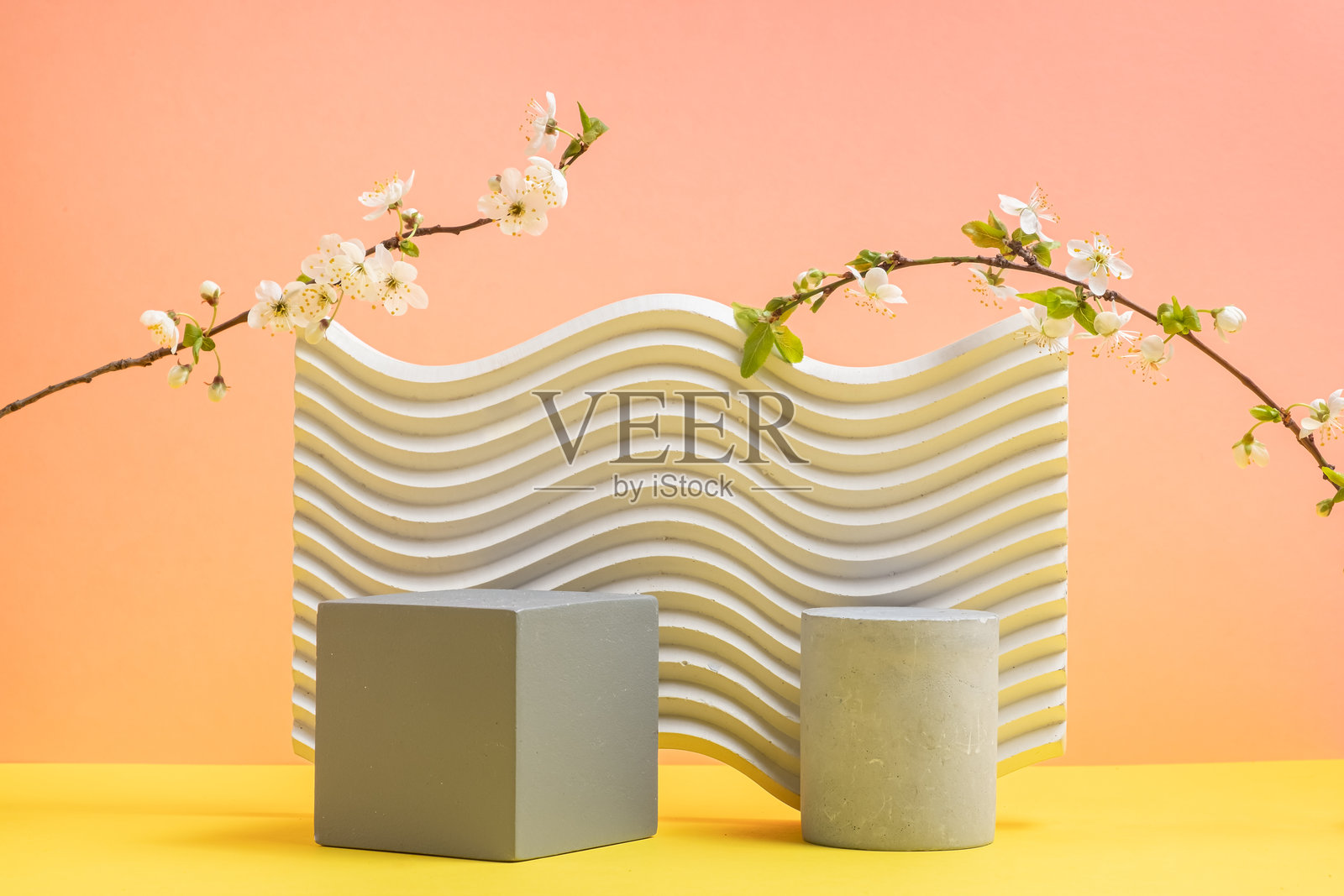 桃黄色背景与几何纹理形状。立方体的灰色讲台和樱花枝。仍然生活。春天的概念照片摄影图片