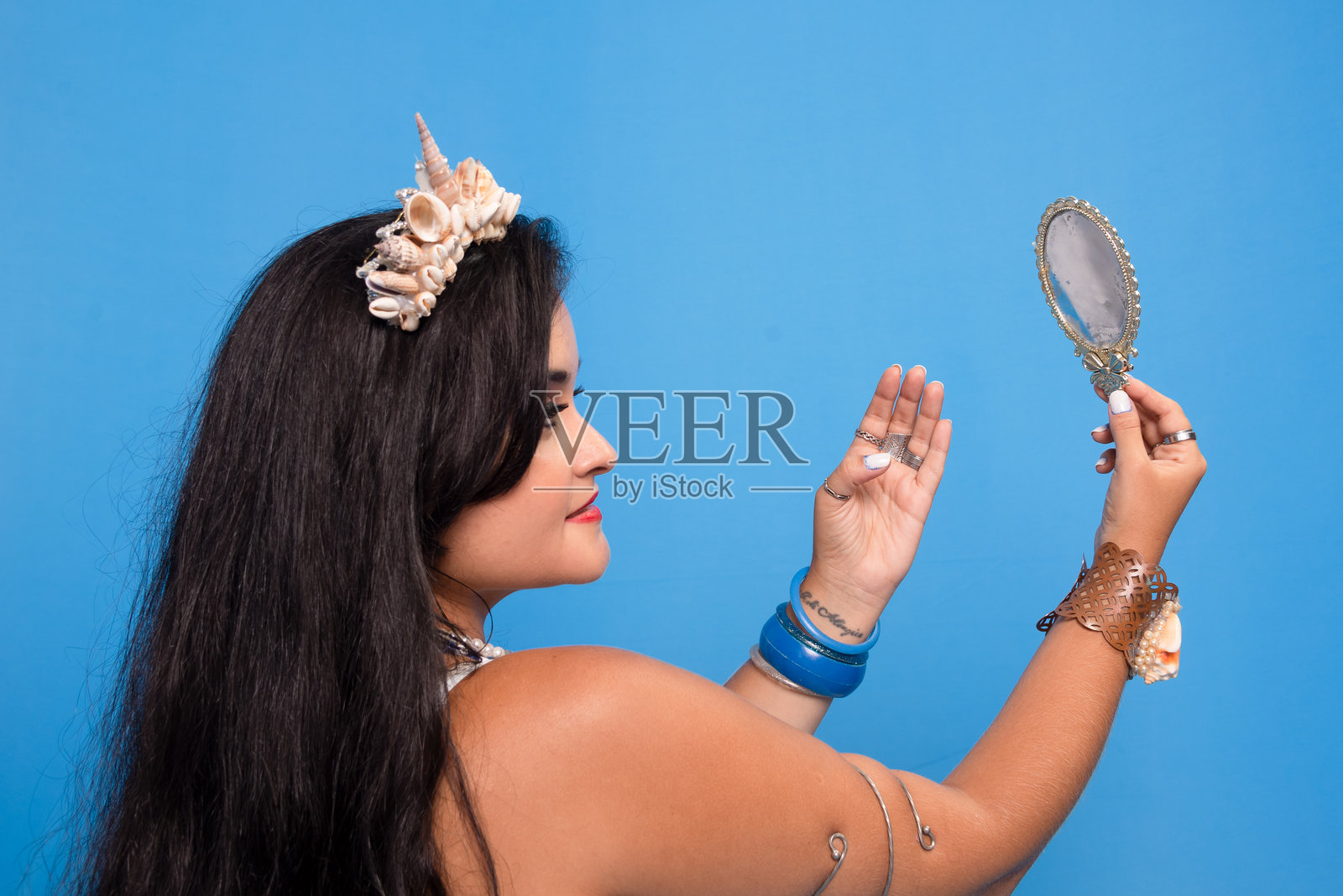 半封闭的美丽的肖像，黑色头发的女人在蓝色的背景，拿着镜子，看着镜子。照片摄影图片