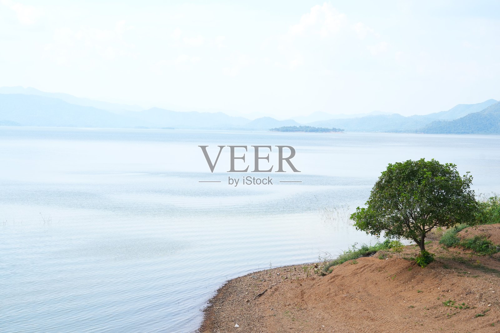 在阳光明媚的日子里，绿色的树在云上的天空，湖和山的背景。清澈的湖水，小小的波浪，在泰国的噶叻山国家公园的湖岸。照片摄影图片