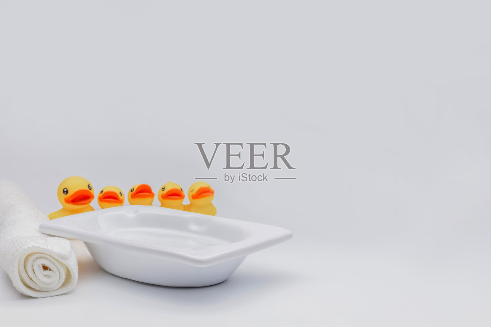 现代的白色浴缸里有肥皂泡，小的黄色橡皮浴鸭浴泡沫和毛巾附近的背景。照片摄影图片