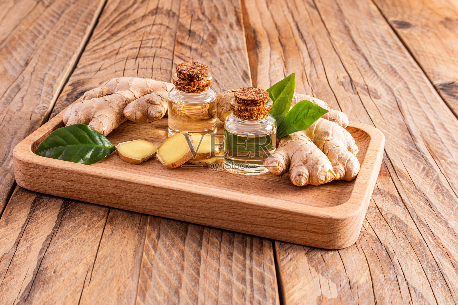 天然姜根油在两个玻璃瓶与木托盘和木桌软木盖。家庭烹饪油的概念和家庭身体护理照片摄影图片