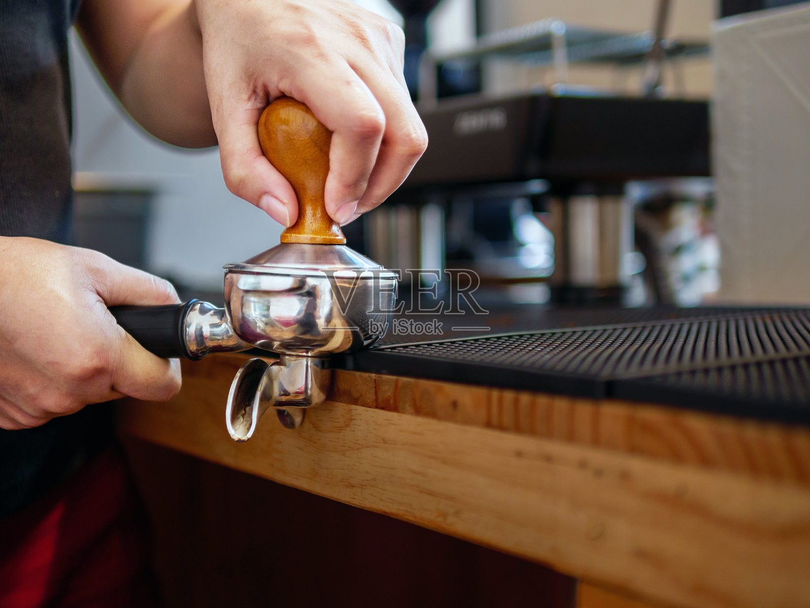 咖啡师拿着咖啡过滤器和咖啡捣碎机制作浓缩咖啡的手。咖啡店里的咖啡师用捣碎机压榨咖啡粉照片摄影图片