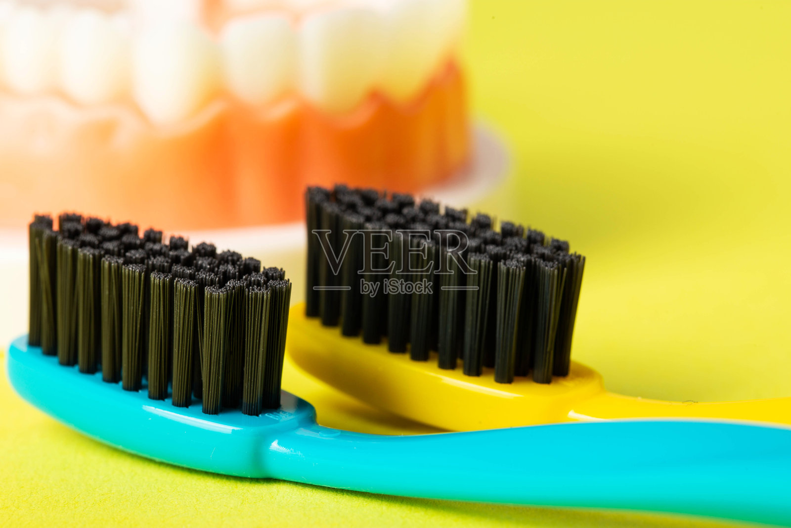 黄色背景上的两支黑炭硬刷毛牙刷，特写。口腔卫生和牙齿清洁的概念，宏观。照片摄影图片