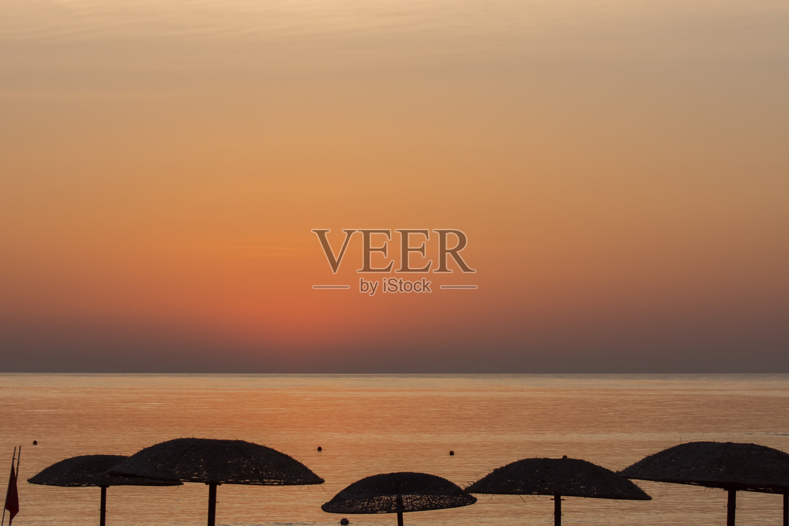 日出前一秒，海滩上有很多遮阳伞，天空是橘红色的照片摄影图片