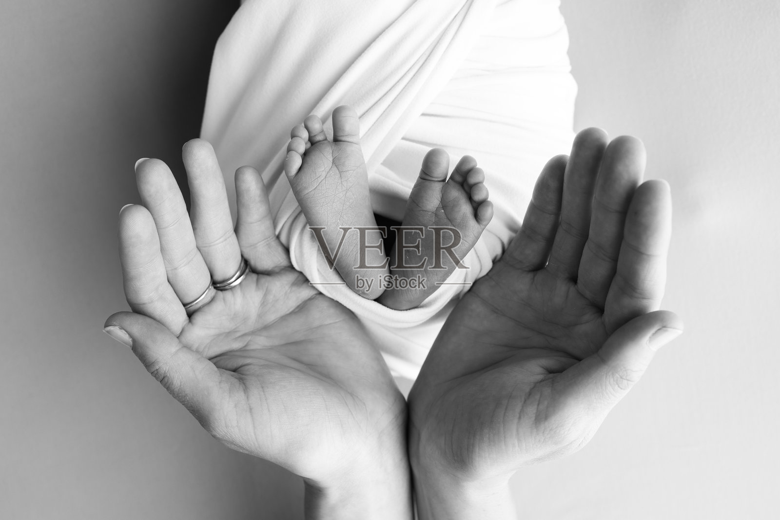 父母的手掌，父亲和母亲握住新生婴儿的腿和脚。新生儿的脚、脚跟和脚趾特写。专业微距摄影。黑色和白色。照片摄影图片