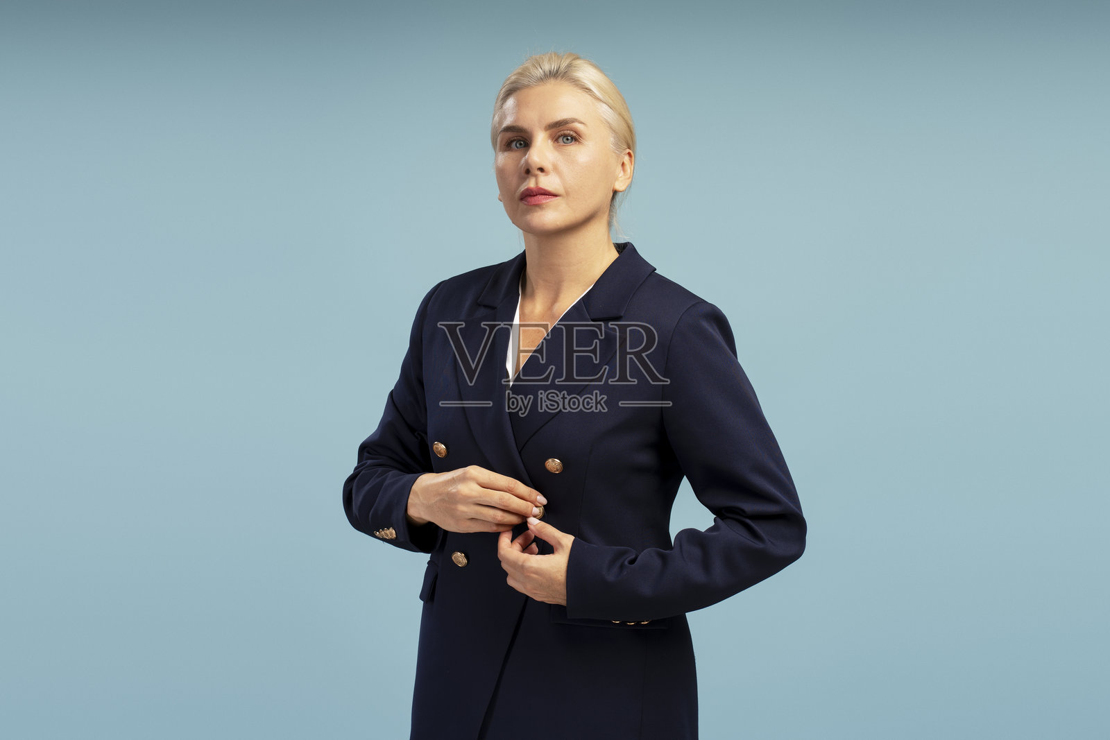 优雅的女商人正在蓝色背景下扣上她的西装外套照片摄影图片