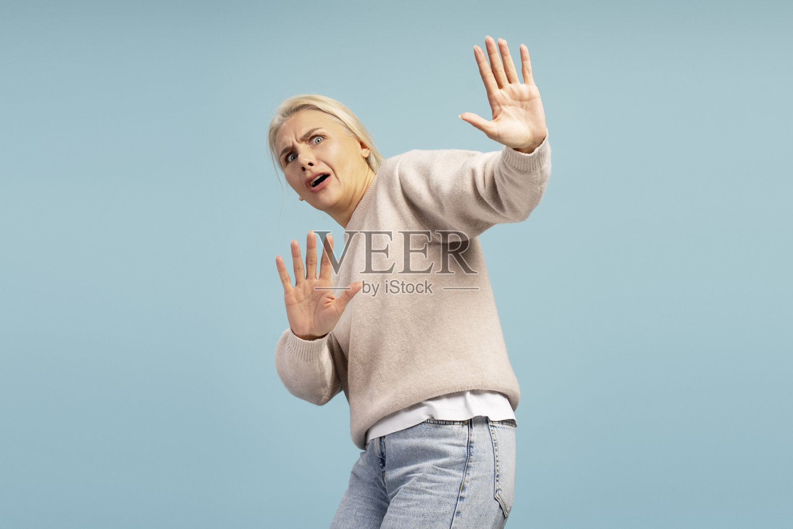 害怕的女人双手举起保护自己，背景为蓝色照片摄影图片