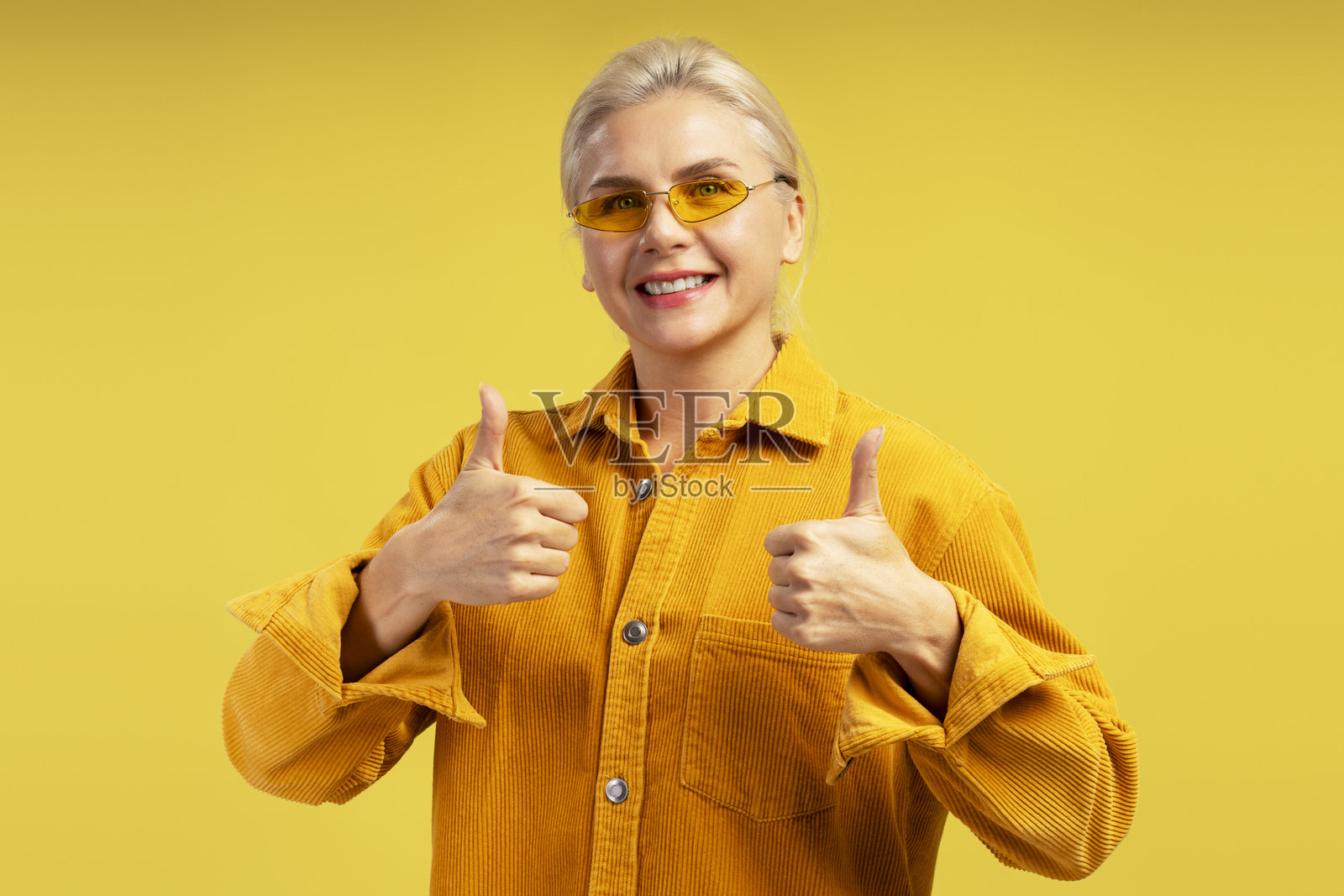 微笑的女性在黄色背景下竖起大拇指照片摄影图片