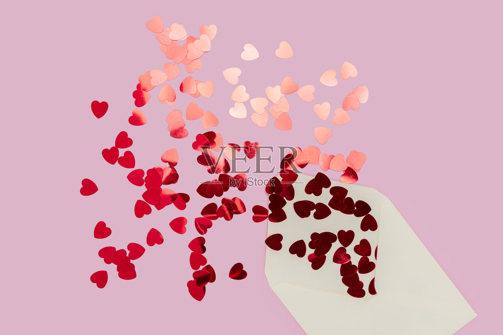 奶油色信封洒落出心形图案，背景为粉色照片摄影图片
