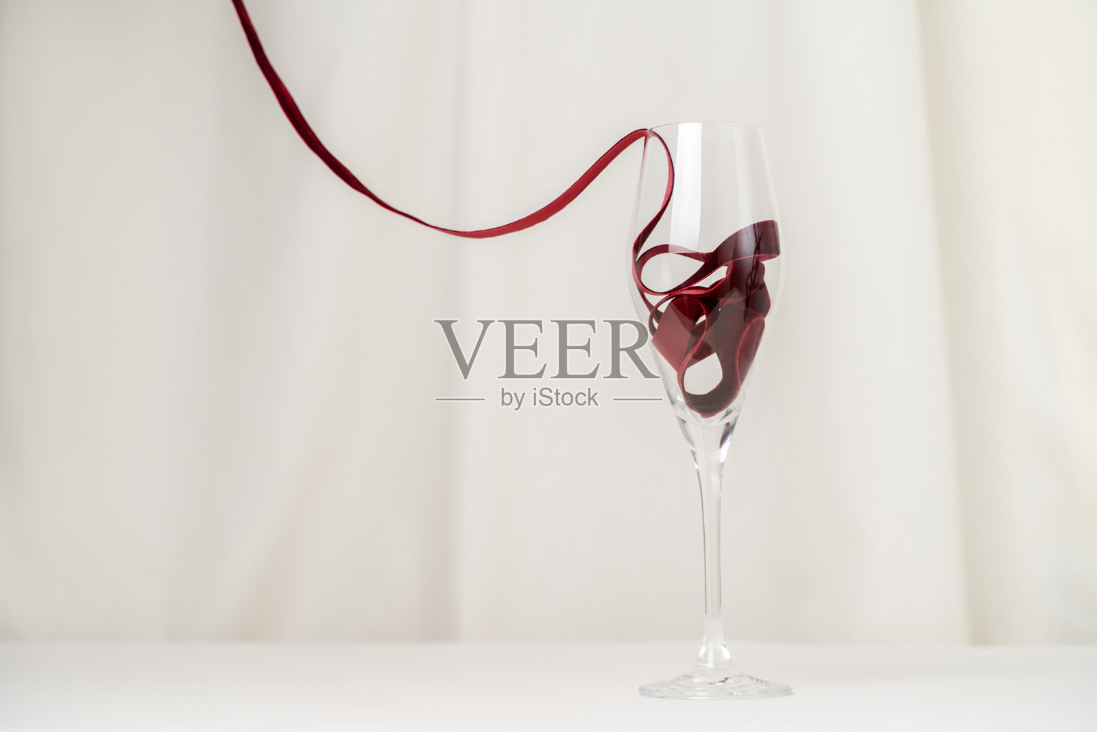 简约的酒杯和红色天鹅绒丝带在奶油色背景上照片摄影图片