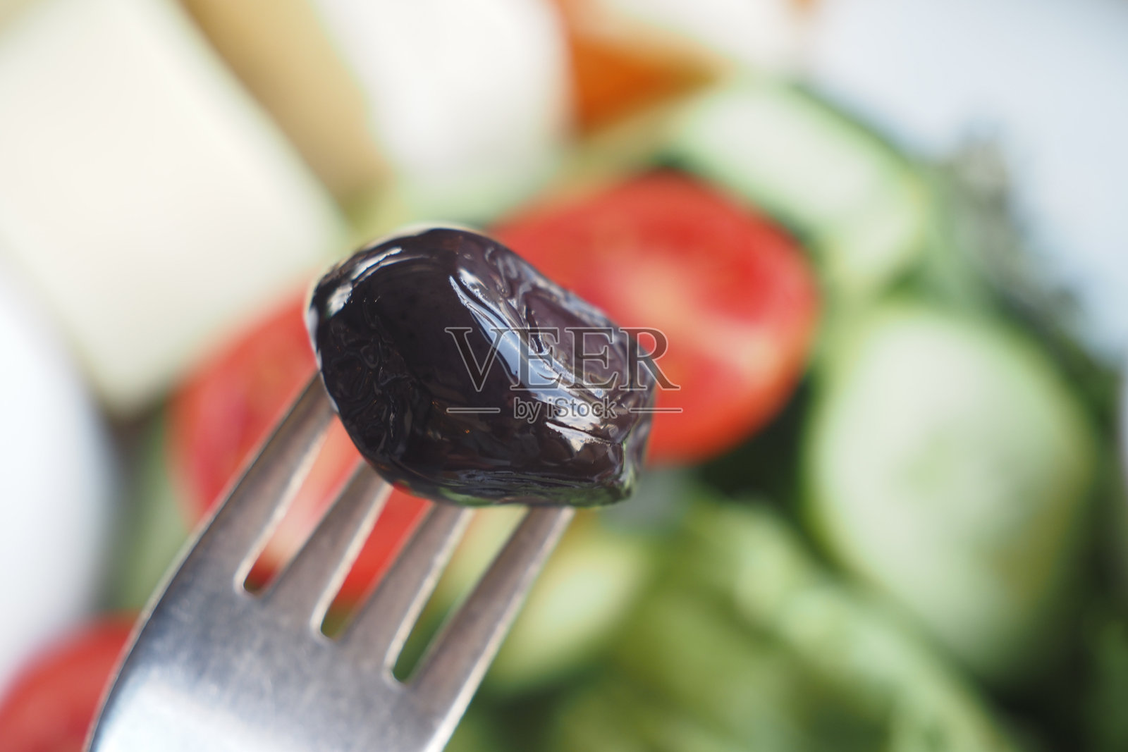 这是一个特写镜头，黑橄榄静静地放在叉子上，背景是沙拉。照片摄影图片