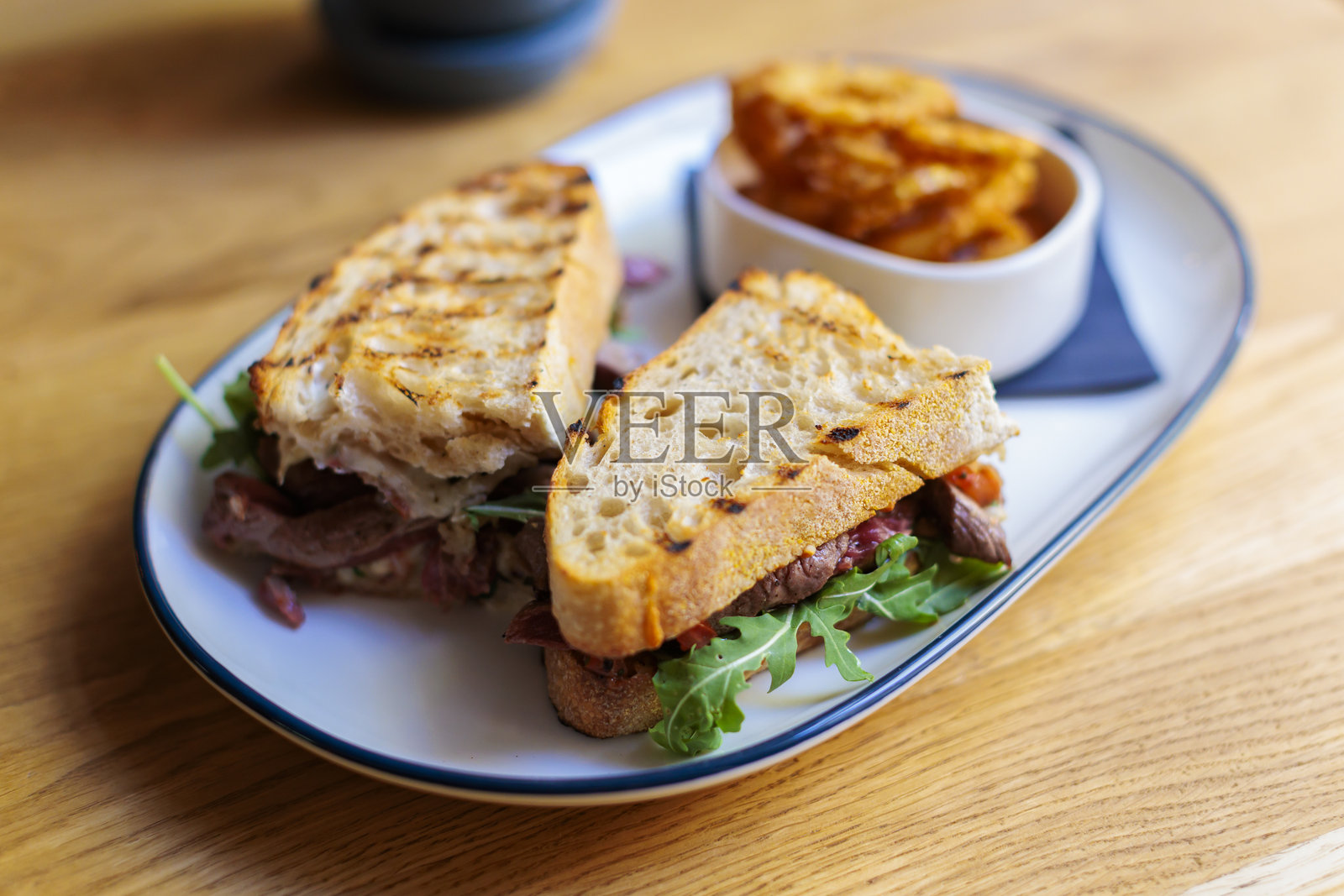 美味的烤牛肉三明治，配有酥脆的洋葱圈和绿色蔬菜，摆放在木桌上照片摄影图片