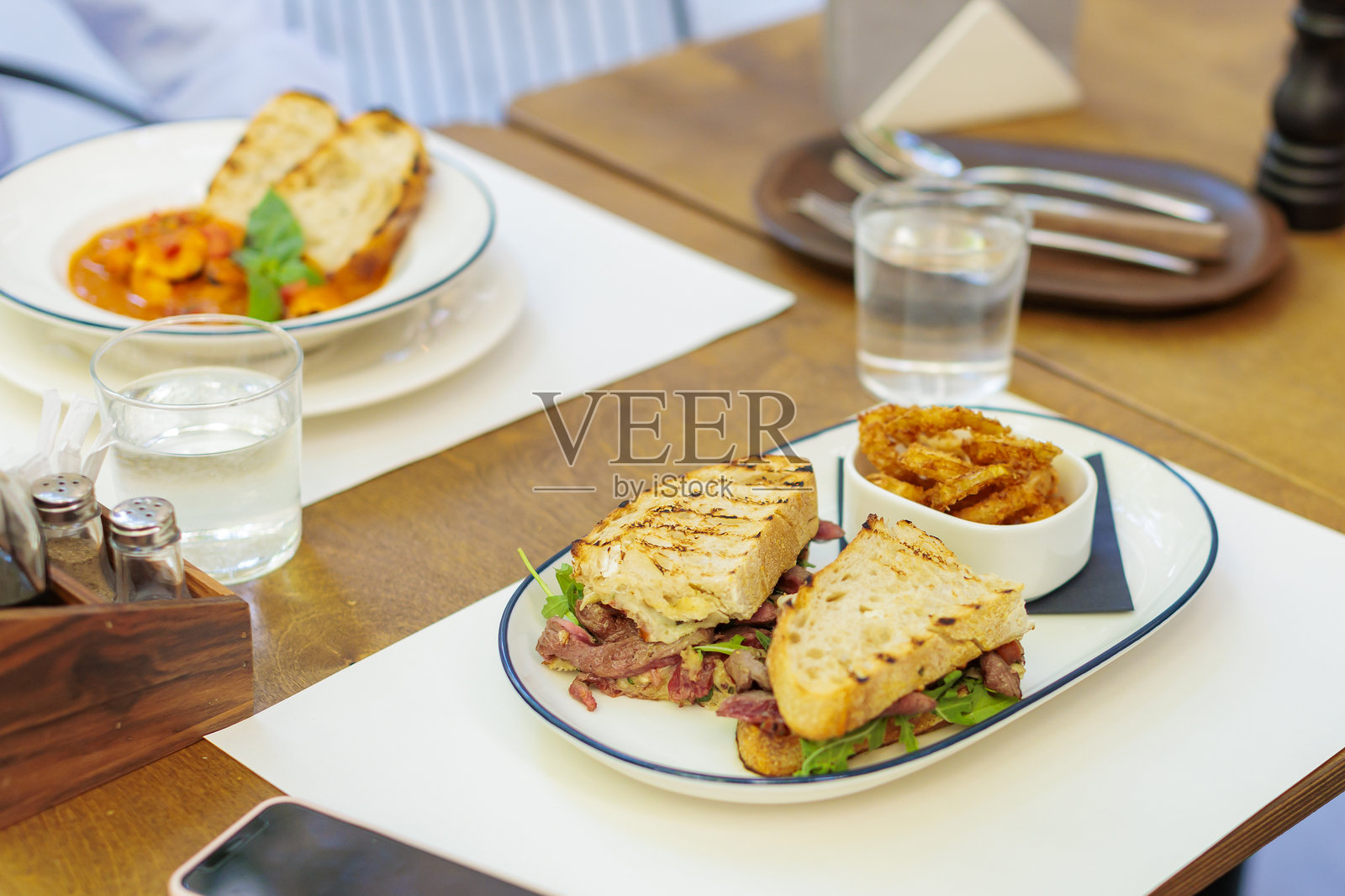 美味的三明治，夹着烤肉和新鲜蔬菜，在繁忙的咖啡馆午餐时光。照片摄影图片