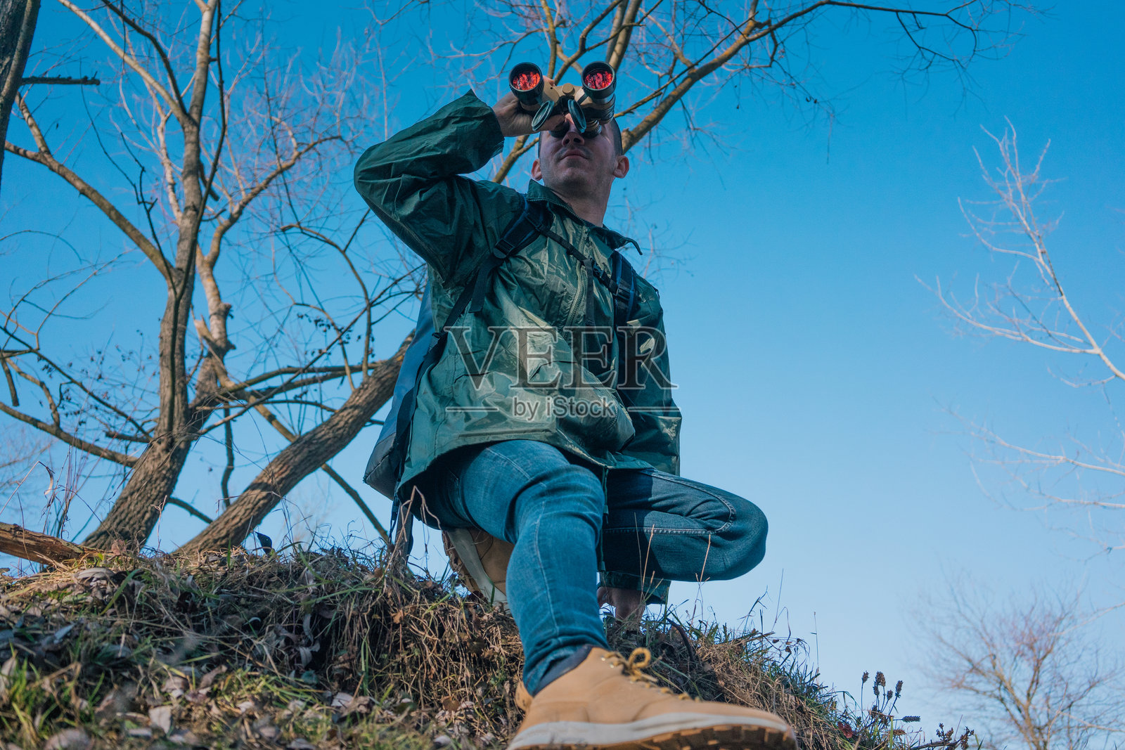 一位年轻帅气的男子背着一个大背包，站在山顶，通过望远镜眺望远方的地平线。他享受探索原始自然，珍惜每一个旅行冒险的时刻。照片摄影图片