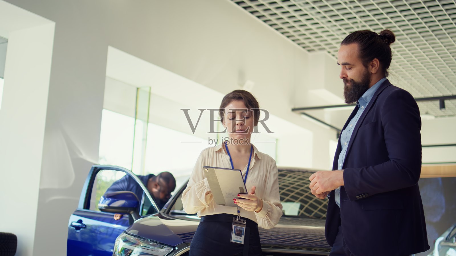 女销售员使用平板电脑向男士展示汽车选择，并提供优惠。照片摄影图片