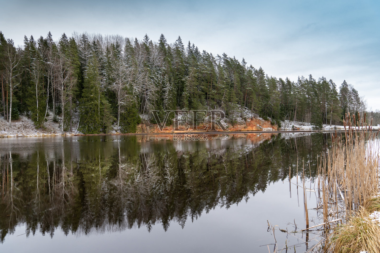 镜面般的水面映照着冬季树木和红色悬崖照片摄影图片