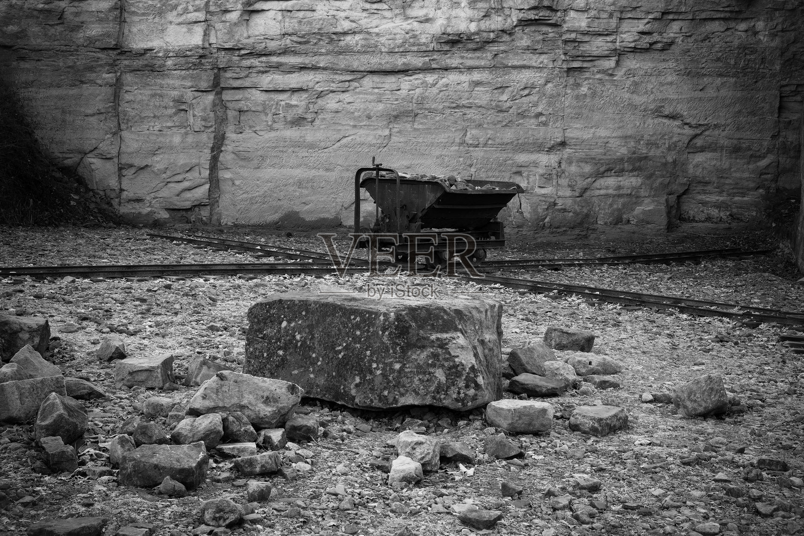 被遗忘的矿车静静地停在一个废弃的采石场，周围是崎岖的地形和陡峭的墙壁，阳光照耀着大地。照片摄影图片
