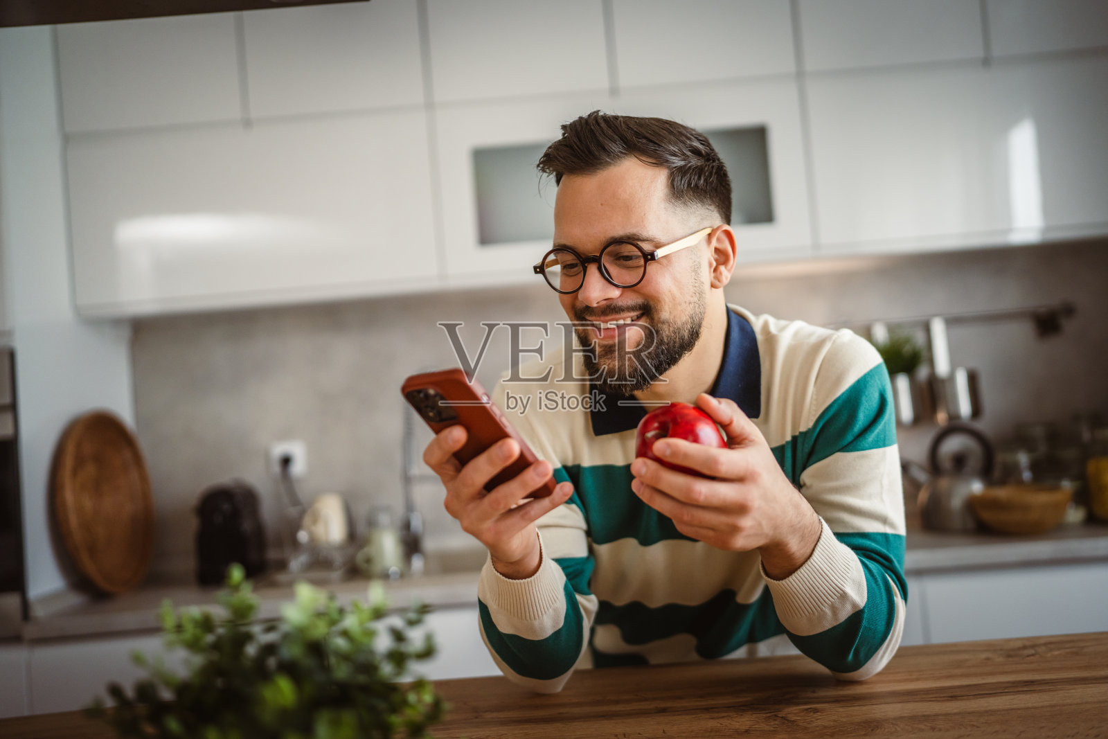 快乐的成年男子吃苹果以补充营养，同时使用手机照片摄影图片