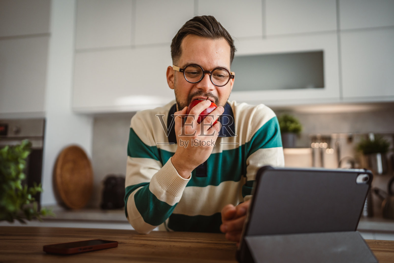 快乐的成年男子在观看平板电脑时吃苹果，注重营养和健康饮食照片摄影图片